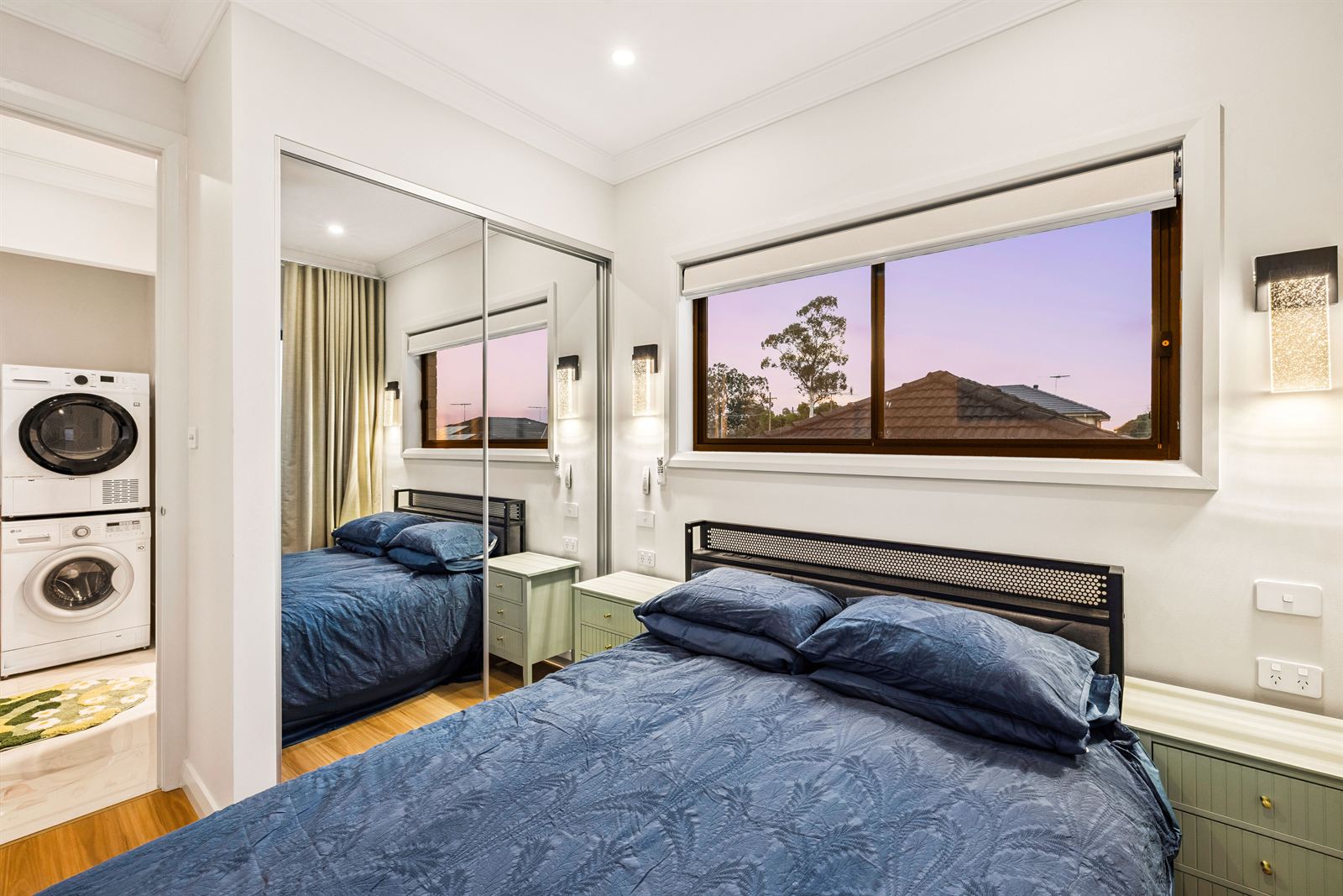 Second bedroom at dusk, with mirrored built-in wardrobes and the laundry through the doorway.