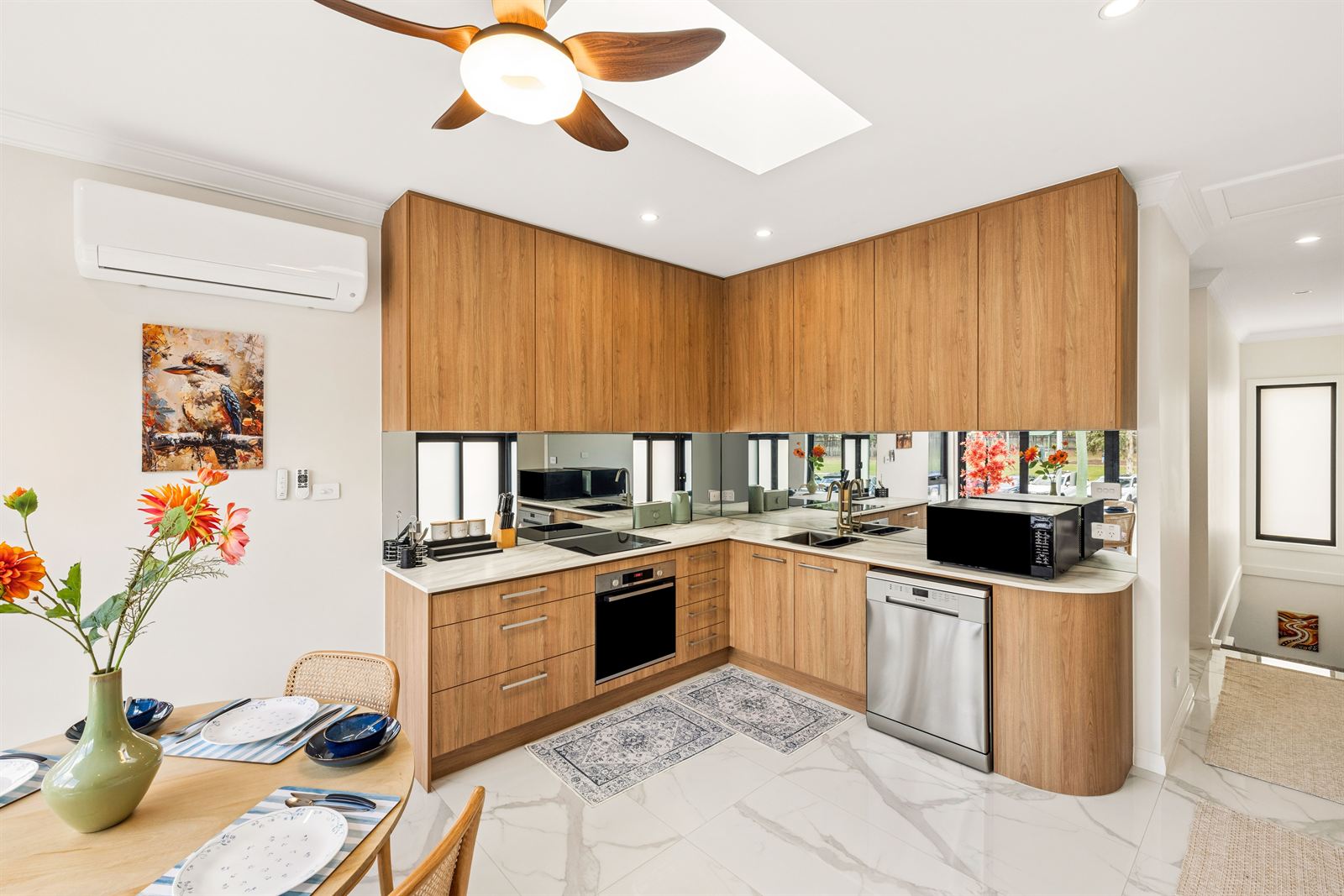 Kitchen with timber cabinetry, mirrored splashback, dishwasher and a skylight overhead.